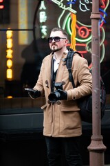 Explorer captures urban life while dressed in a stylish coat, standing next to a neon-lit...