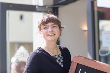 Smiling young woman holding a chalkboard sign outside a modern building. Germany