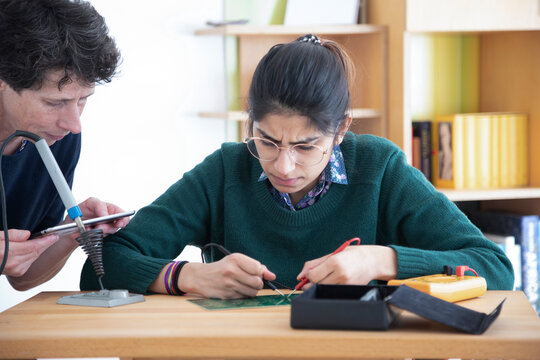 Two people working on electronics at a wooden table, focusing and collaborating on a project, Germany