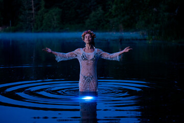 Woman standing in calm water wearing a crocheted dress and floral crown with arms outstretched. WA, USA
