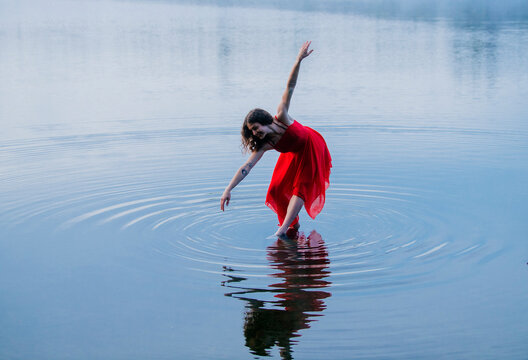 Woman in a red dress gracefully dances on a tranquil lake with rippling water reflections. WA, USA