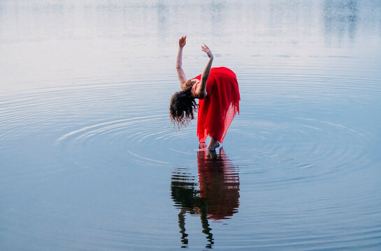 Woman in a red dress gracefully dances on a tranquil lake with rippling water reflections. WA, USA