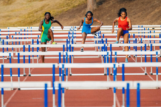 Three athletes in colorful sports attire hurdling on an outdoor track in a competitive race. USA
