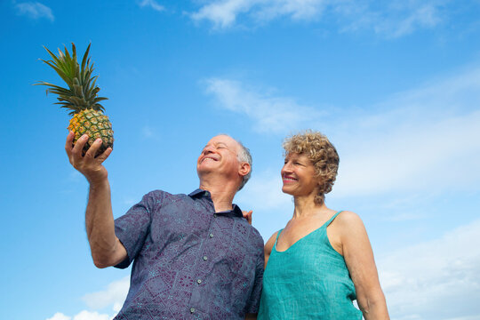 Older couple enjoying a sunny day with a pineapple in hand against a blue sky. Kepaniwai Park, Wailuku, Hawaii