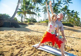 Senior couple practicing yoga on a sandy beach surrounded by palm trees in bright sunlight. Kepaniwai Park, Wailuku, Hawaii