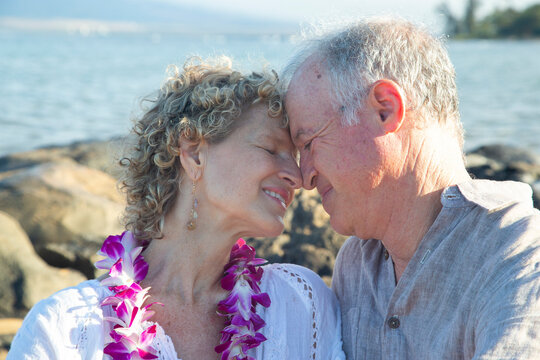 Elderly couple embracing affectionately by the ocean with floral garlands. Kepaniwai Park, Wailuku, Hawaii