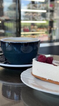 A cup of coffee and a cake with berries in a pastry shop. Vertical