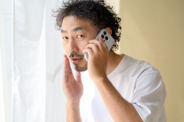 窓際でスマホを持ち内緒話をする髭の日本人男性