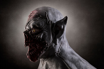 Portrait of a monster with sharp fangs over dark foggy background. Silicone mask was used in this photo.