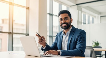 Fototapeta premium Professional Young Man Wearing Blue Suit Sitting at Desk with Laptop in Bright Modern Office