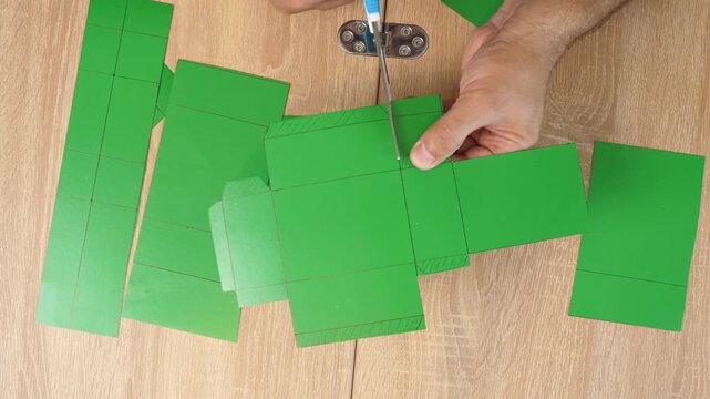 Hands folding and gluing cardboard cutouts, assembling parts of paper model for creative DIY craft project.