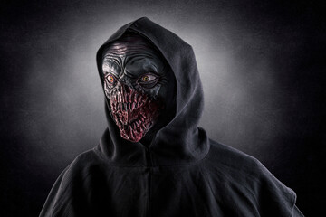 Portrait of a monster with sharp fangs with hooded cape over dark foggy background. 