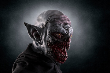 Portrait of a monster with sharp fangs over dark foggy background.