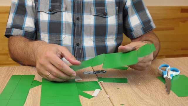 Hands folding and gluing cardboard cutouts, assembling parts of paper model for creative DIY craft project.