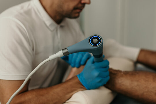 Physiotherapist using shock wave therapy machine on patient's foot