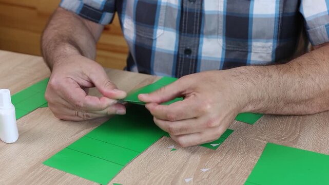 Hands folding and gluing cardboard cutouts, assembling parts of paper model for creative DIY craft project.