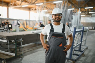Happy bearded Indian male factory worker in special uniform and white hard hat holding aluminum...