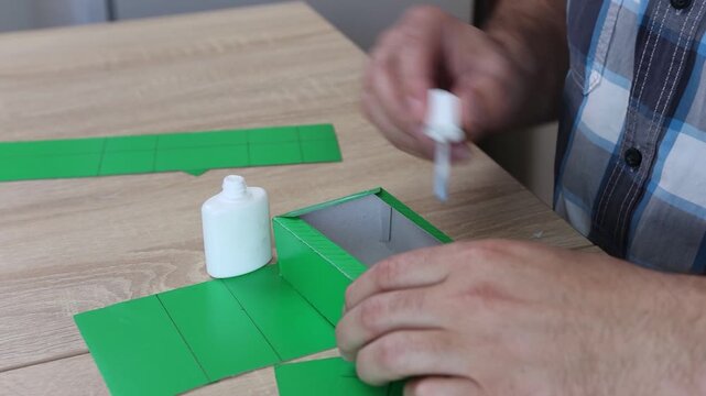Hands folding and gluing cardboard cutouts, assembling parts of paper model for creative DIY craft project.
