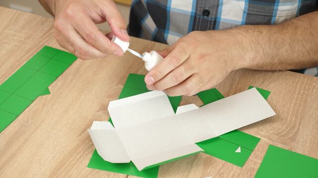 Hands folding and gluing cardboard cutouts, assembling parts of paper model for creative DIY craft project.