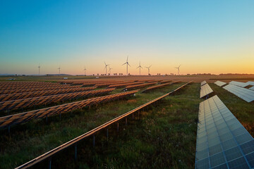 Rows of solar panels and wind turbines in countryside field at sunset. Concept of renewable energy,...