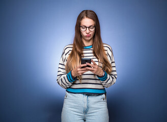 Confused young woman holding the mobile phone, isolated on blue background. Female person with...