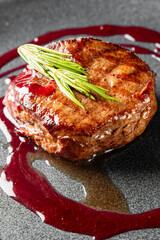 Grilled beef steak with glossy red sauce and fresh rosemary garnish on a dark plate, close-up view of gourmet meat dish