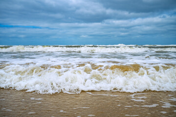 Breaking wave from a worm's-eye view, rolling directly toward the camera. Surf with foam and spray on the sandy beach of Norderney in the Wadden Sea National Park (East Frisian Islands, Germany).