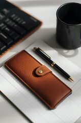 Elegant brown leather pen case resting on a notebook beside a black pen and coffee cup