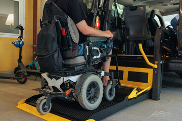 Person with disability is on a wheelchair entering a transportation vehicle via lift in a modern facility during daytime.
