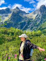Naklejka premium Young woman standing and admiring mountains and lush greenery valley view. Hiking trail in High Tatras, Slovakia, Zelene Pleso (Green lake)