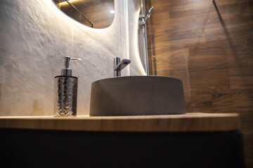 Stylish stone sink in a wooden countertop against the background of a mirror with diode lighting...