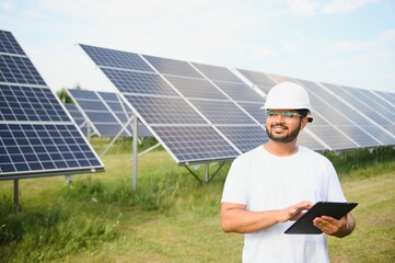 An Indian male engineer working on a field of solar panels. The concept of renewable energy