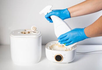 Man in blue gloves spraying descaler, mold and odor remover into humidifier on white background....