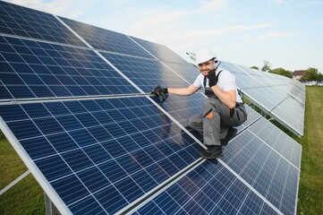 Side view of male worker installing solar modules and support structures of photovoltaic solar...