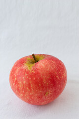 Single fresh red apple with natural texture on a clean white tablecloth. Minimalist concept of healthy eating, organic food and wellness diet. Top view with ample copy space for design.