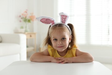 Curious little girl in bunny ears at white table indoors