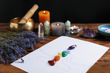 Human drawing with gemstones placed on chakras, lavender flowers on wooden table, closeup