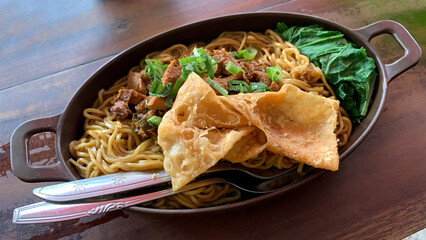 A plate of chicken noodles served with a fried wonton on a wooden table