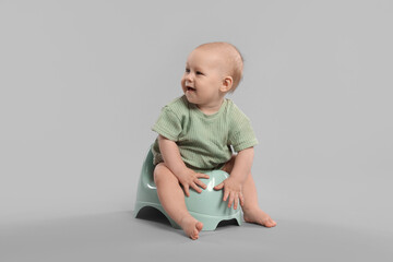 Cute little baby sitting on potty against light grey background