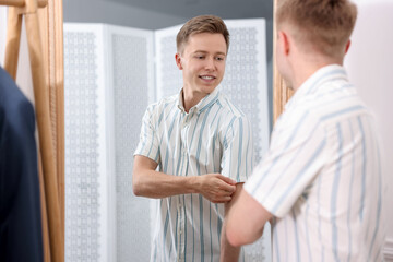 Fototapeta premium Getting ready. Young man trying on clothes near mirror at home