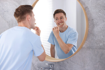 Getting ready. Young man brushing his teeth near mirror at home