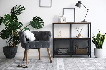 Stylish grey armchair, shelving unit and houseplants indoors. Interior design