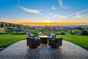 A patio set with chairs and firepit on a custom stone paver tiled terrace above the city of Spokane, Washington, USA at sunset.