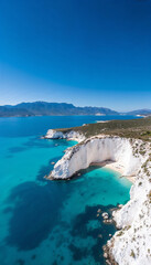 Fototapeta premium Aerial view of a white cliff with a beach and turquoise waters, backed by mountains.