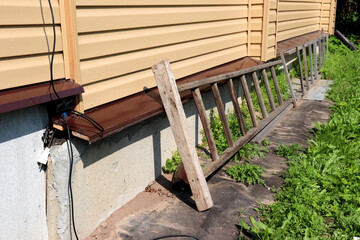 Wooden portable ladders lie against the wall of a rural house in a garden on a sunny summer day -...