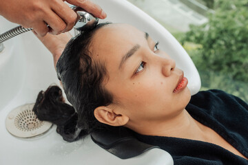 Southeast Asian woman calmly seated at a salon sink while her hair is rinsed in preparation for a...