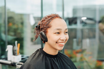 Southeast Asian woman with her hair fully coated in red dye during a professional salon coloring session, waiting for processing.