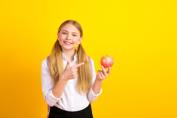 Smiling schoolgirl holding an apple on a yellow background, promoting education and healthy...