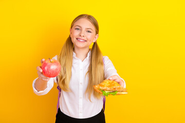 Blonde schoolgirl holding an apple and sandwich on yellow background promoting healthy eating...