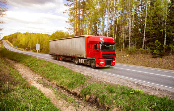 Red truck with tarpaulin semitrailer transports cargo on country road. Concept of forwarding driver, cargo transportation and business, industry
